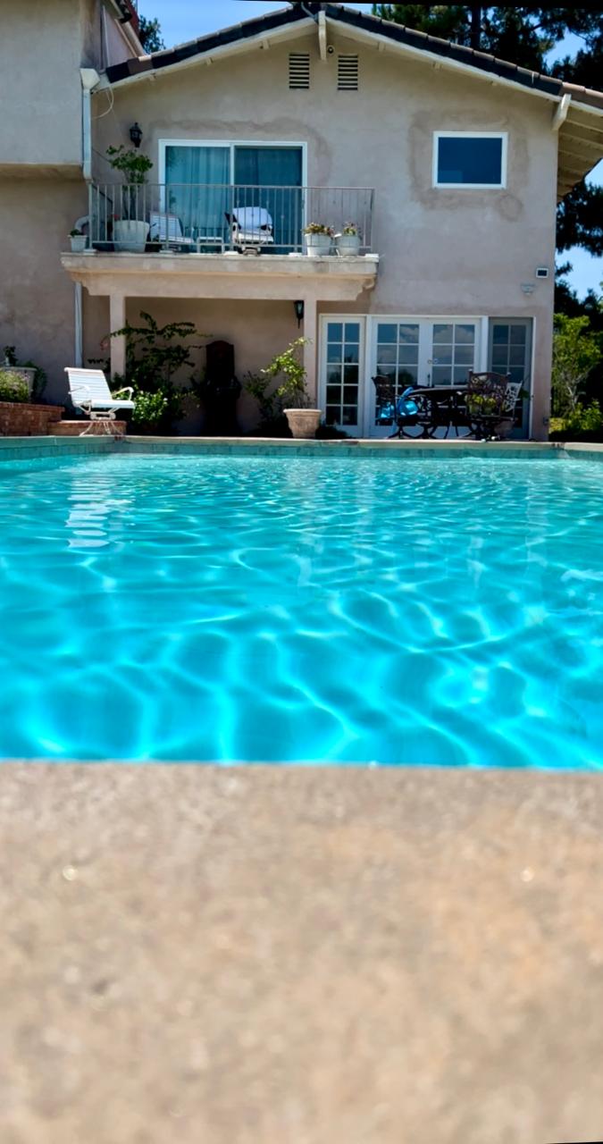 Crystal-clear backyard pool in front of a two-story hillside home serviced by KLUG Pool Services